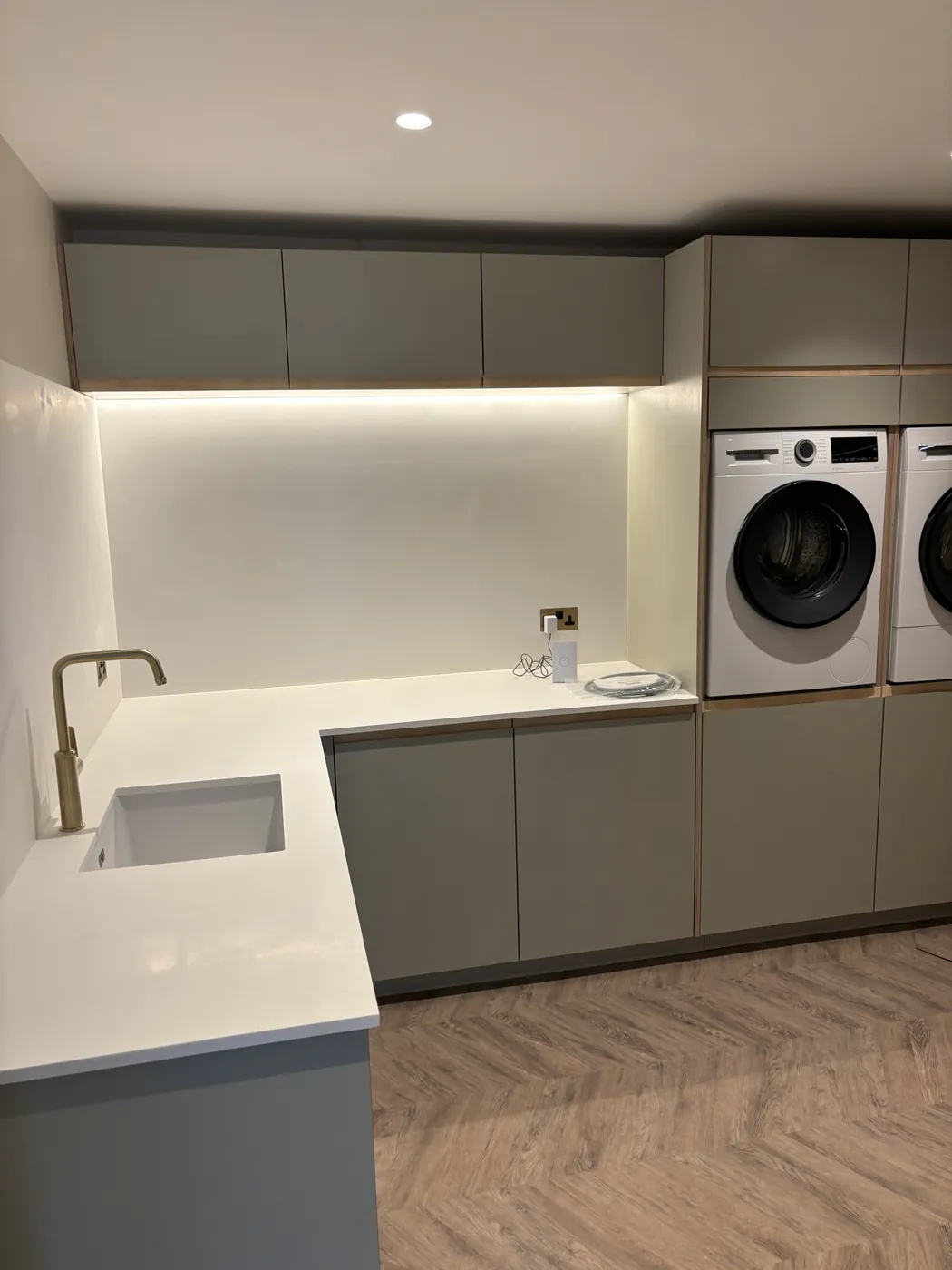 Utility room with grey units, a pale worktop and stacked appliances