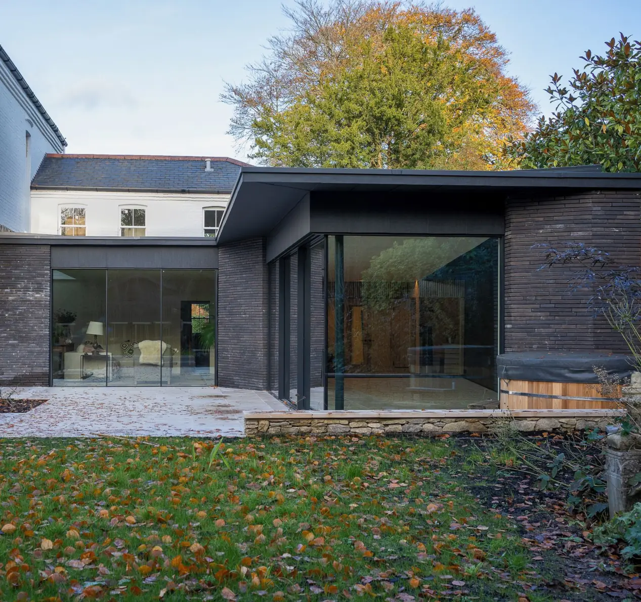 Pool extension in black linear brick with frameless glazing, beside the white period house