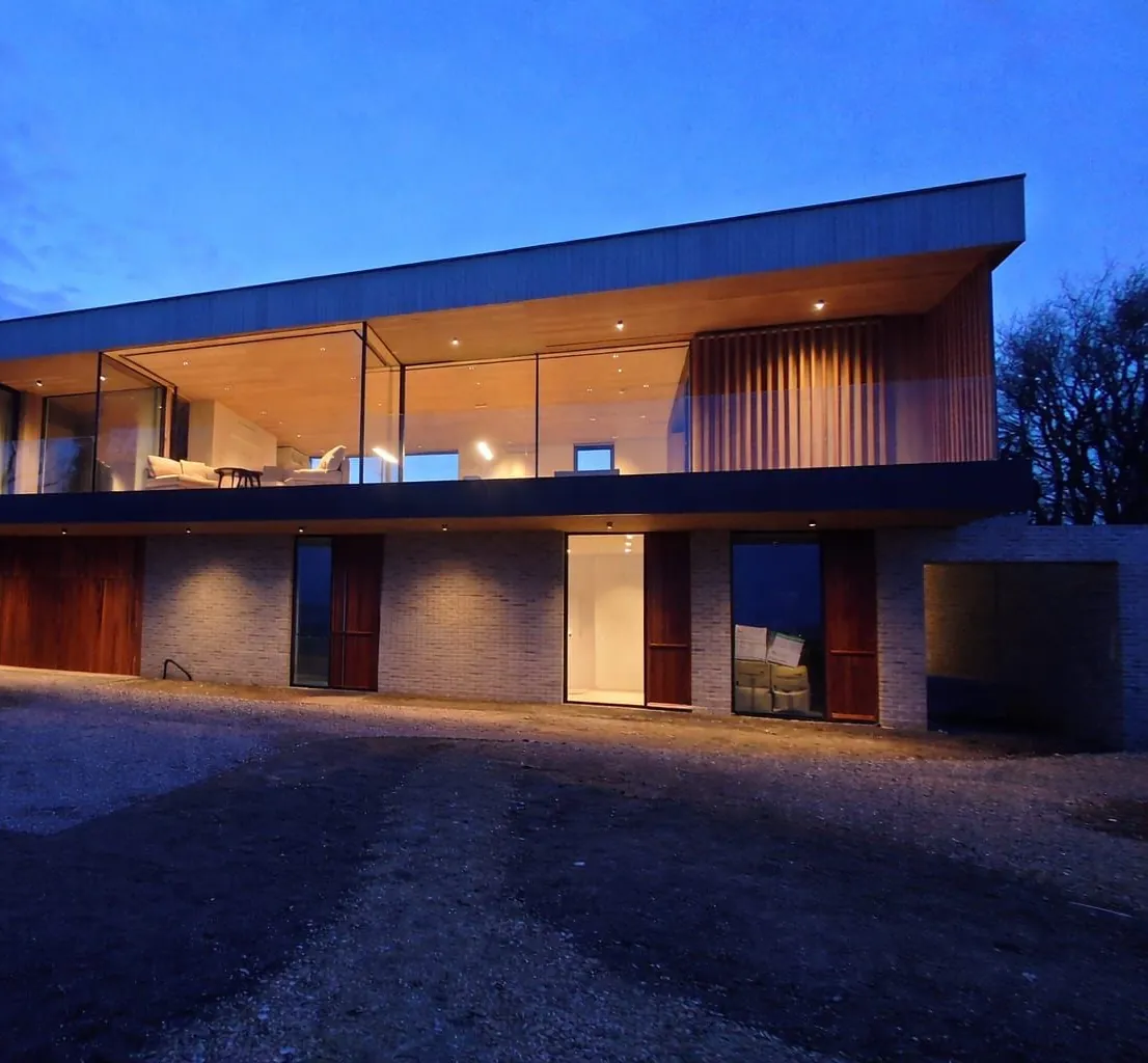 The house at dusk, lit from within behind its long first-floor glazing