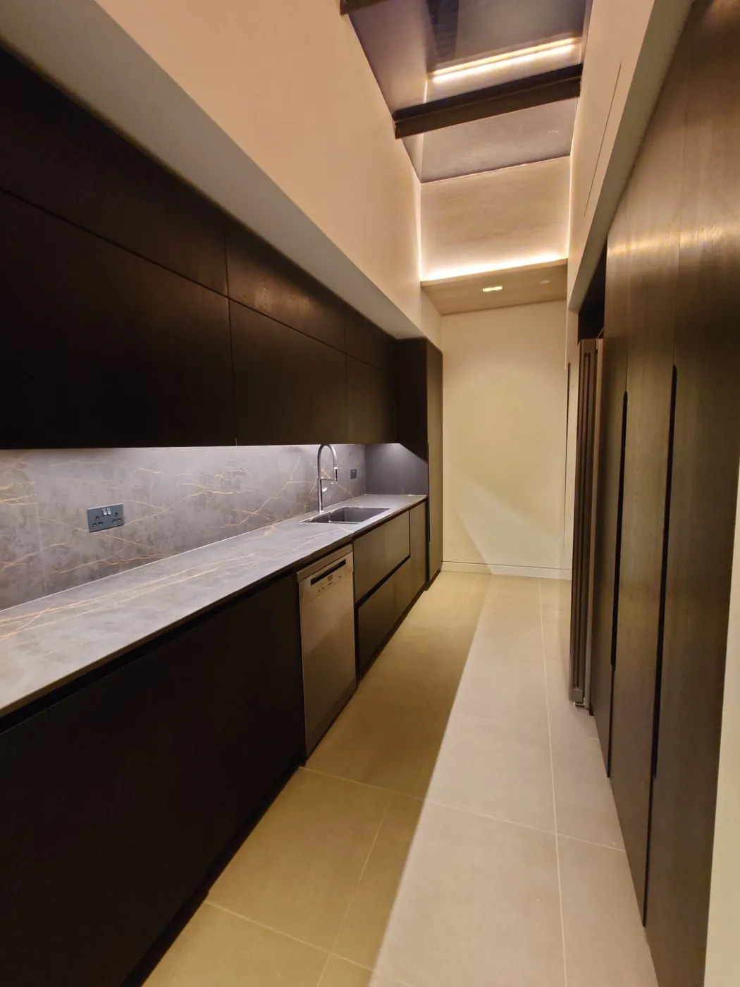 Galley kitchen in dark joinery, with a stone worktop and a lit shelf