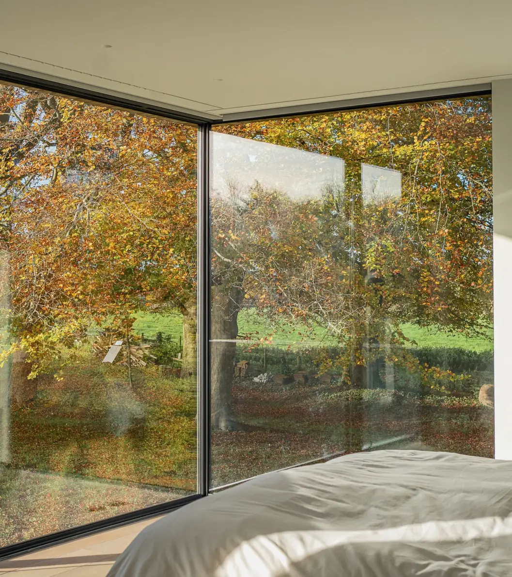 Frameless corner glazing in a bedroom, looking out to autumn trees
