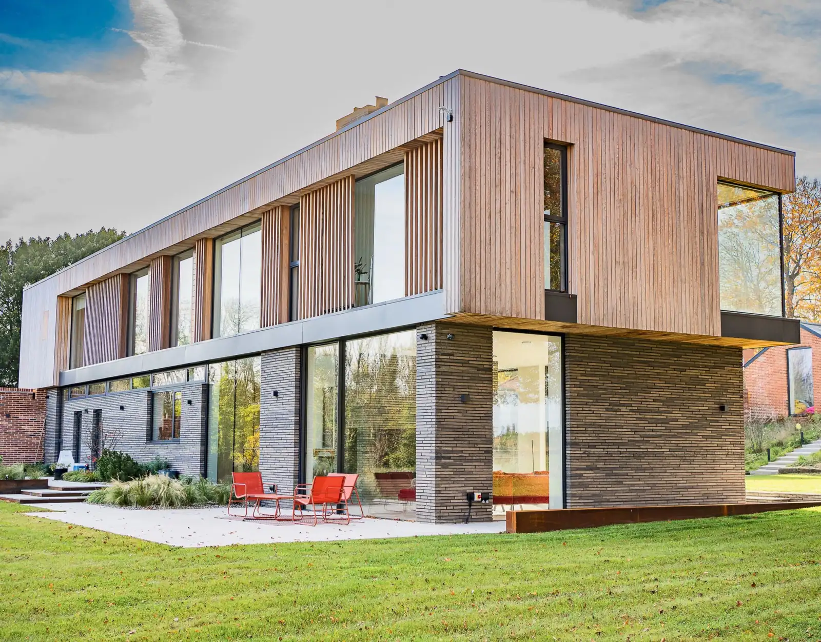 Two-storey contemporary house with a vertical timber-clad upper storey cantilevered over a dark brick ground floor