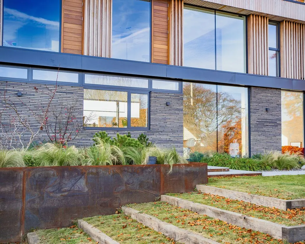 Garden elevation of dark linear brick and timber cladding above steel-edged planters and grass steps