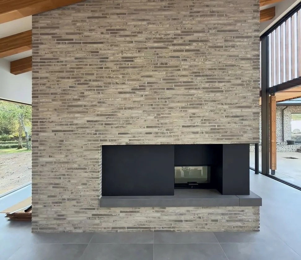 Double-sided fireplace in long, slim brick under exposed timber rafters